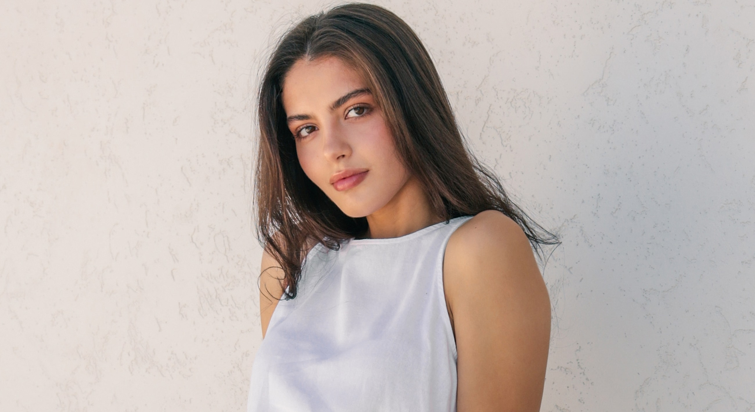 Young woman with long hair against a textured wall.